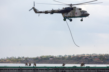 Soldiers descend from a helicopter to a barge