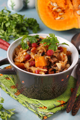Vegetable stew with hunting sausages in a ceramic pot on a light blue background, Vertical orientation
