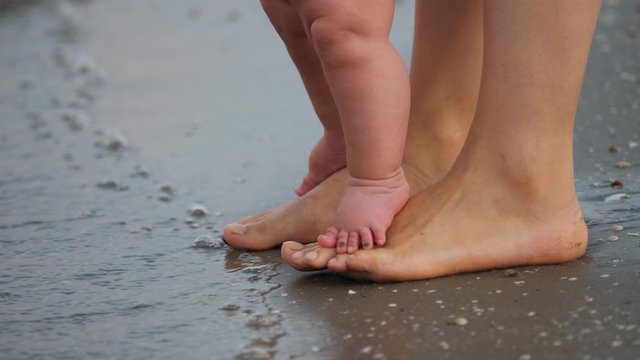 Little baby feet on mother learn to walk, first step at sea shore
