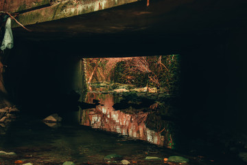 Fototapeta na wymiar A Shallow Creek Flowing Unnder a Concrete Bridge Surrounded by Foliage and Rocks