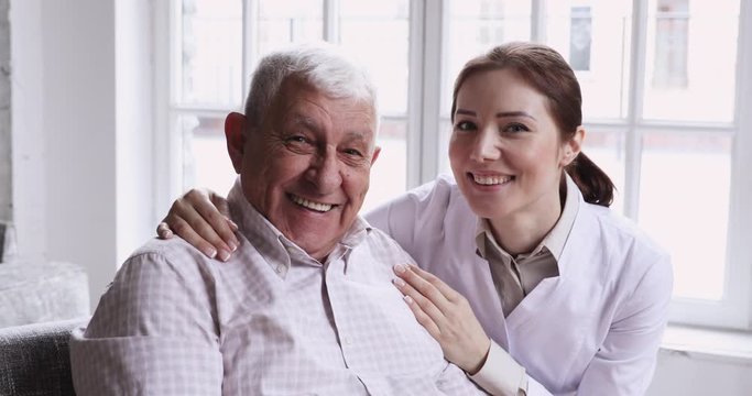 Caring smiling female caregiver embracing happy senior patient, closeup portrait