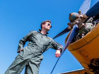A handsome young pilot standing next to the propeller
