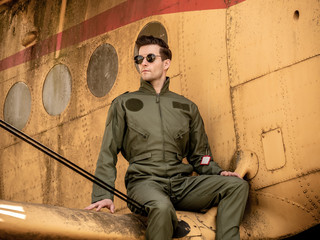 A handsome young pilot sitting on the wing of a plane