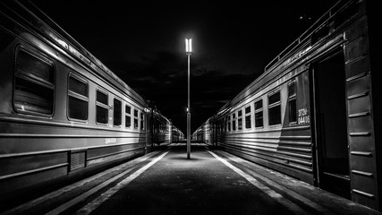 A lone lantern illuminating an empty night platform with waiting train cars.