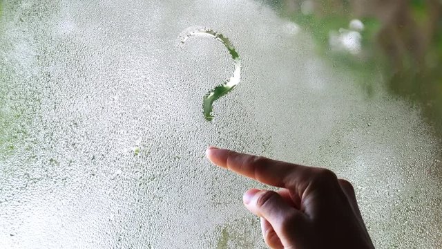 a woman's hand draws a question mark on the fogged glass. concept of the problem and its solution