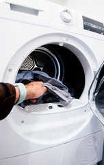Male hand filling the washer dryer machine large open door of the home appliance