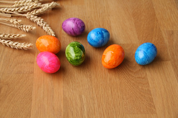 colored boiled eggs are scattered on a natural wooden table, a bunch of bread ears, harvest concept and Easter