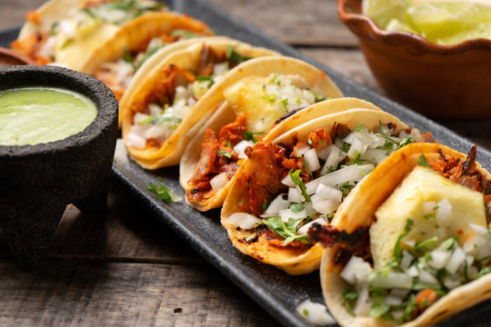 Mexican pork tacos called "Al pastor" with pineapple on wooden background