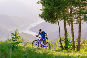 Naklejka premium Mountain biker wearing a blue shirt is pushing his bike through green woods while enjoying the amazing view.