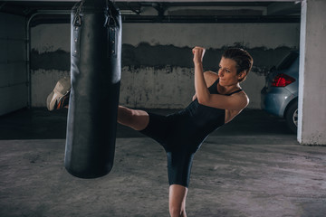 Young sportswoman doing high kick during boxing exercise in a garage.