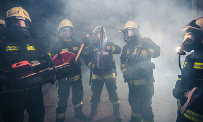 Group of firemen with gas masks standing in the middle of the chainsaw's smoke