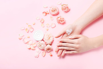 Woman's hands with heart shape created from natural cream. Care about soft, smooth skin. Beautiful fresh roses on pink table.