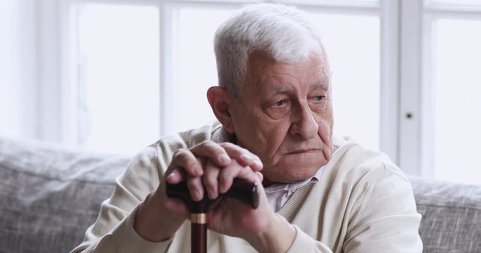 Sad old grandfather hold cane stick sit alone on couch