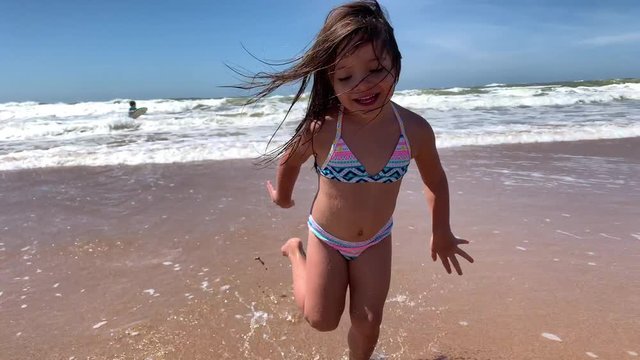 Happy ecstatic little girl running at beach. Joyful kid child runs at sea shore