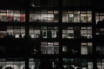 Facade of a business district building, a high rise, at night, in the evening, with only a few...