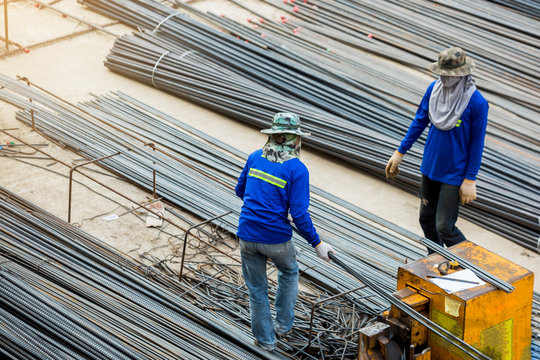 Selective focus to construction worker and many deformed steel bar working with electric iron cutting machine at the construction site. Large scale high rise building construction project.