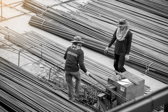 Black and white imahe of construction worker and many deformed steel bar working with hydraulic rebar cutting machine at the construction site. Large scale high rise building construction project.