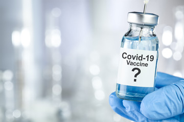 Possible cure concept with a hand in blue medical gloves holding Coronavirus, Covid 19 virus, vaccine vial