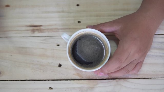 Top view of Person hand steering coffee in a cup with spoon. Breakfast morning of a cup hot black coffee on wooden background. footage b-roll scene 4k. home made coffee. 