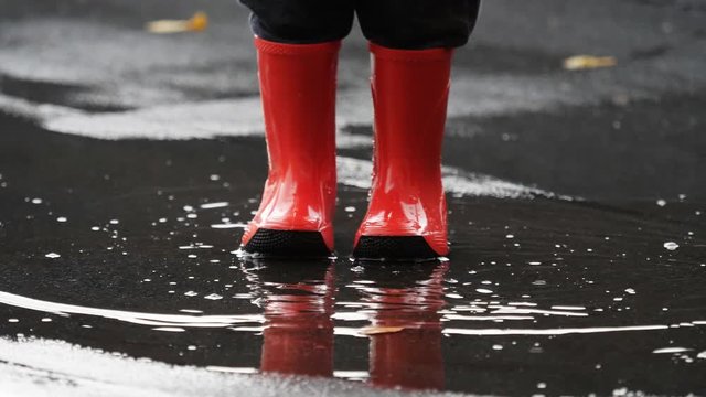 Detail of red rubber boots splashing muddle water, easy and free childhood