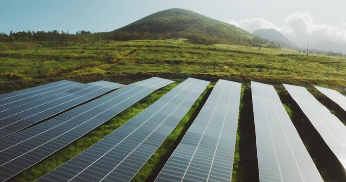 Aerial view flying over a solar panel farm at sunrise with verdant green mountains in the background, the future of green renewable energy is the sun