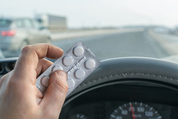 driver hand holding a bag of pills while driving on the highway
