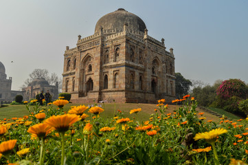 A mesmerizing view of shish gumbad monument with yellow flowers at lodi garden or lodhi gardens in a city park from the side of the lawn at winter foggy morning.