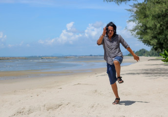 Asian Thai middle aged man long hair with funny face running on beach and sea ocean sand blue sky clouds. Thai adult with funny energy action and natural background.
