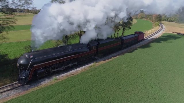 Aerial frontal close view of an antique restored steam locomotive traveling thru the countryside blowing black smoke and steam