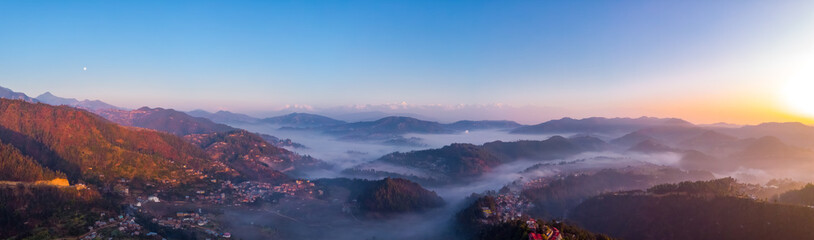 Panorama Moody Dramatic view of mountains covered in fog during sunrise with Great Himalaya Range in the backdrop.