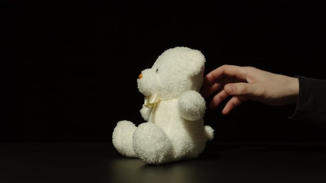 Man Grabbing Small Plush Bear Toy Quietly Off The Black Surface