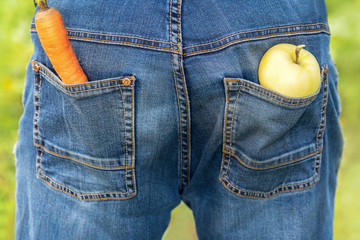 .Carrot and Apple. Men's jeans have an Apple and a carrot in their pockets. Rear view. Healthy...