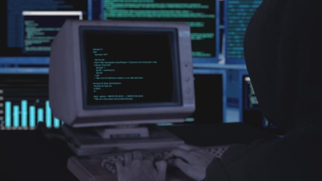 Hooded man using an old computer for hacking