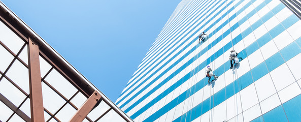 Group of workers cleaner cleaning windows on high rise building skyscraper  over blue sky