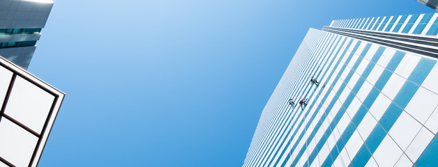 Group of workers cleaner cleaning windows on high rise building skyscraper  over blue sky
