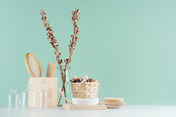 Elegant natural beige toiletry for bathing with wooden decoration -  comb, brush, soap, glass vases in green aqua mint interior, white wood table.