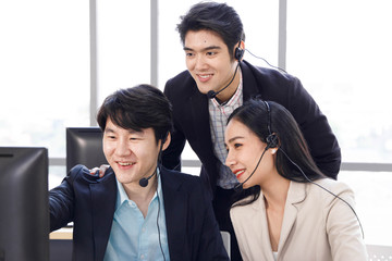 Three happy Asian call center operator agent working together and help each other. Concept for business, teamwork, office lifestyle.
