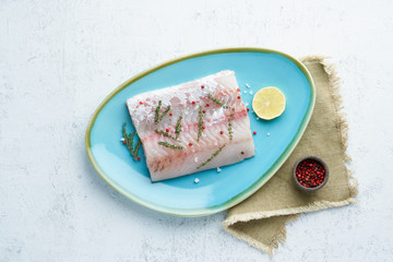 Fillet of raw white walleye fish on a blue plate on a white background. Whole piece of fresh fish