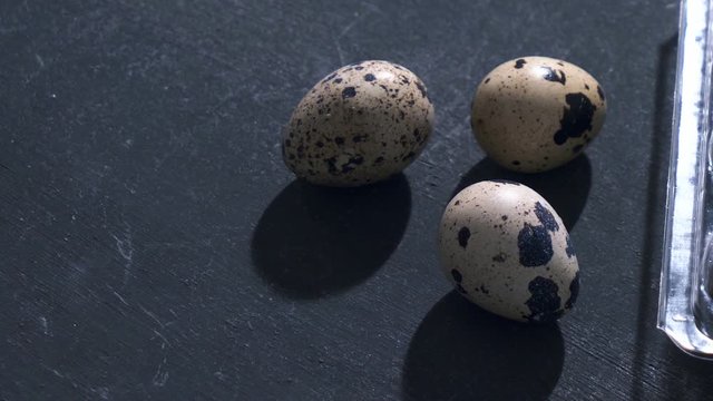raw quail eggs and plastic box on gray background