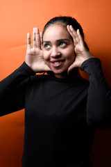 Arabic young woman making frame gesture with hands over orange background. Portrait of a happy smiling woman framing her face with her hands isolated

