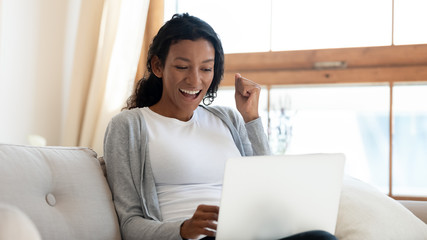 Overjoyed biracial woman triumph reading good news on laptop