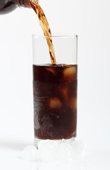 Pouring cola from plastic bottle into glass with ice cubes. Isolated on white background.