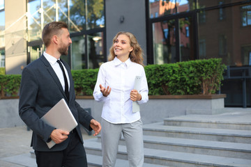 Office colleagues talking outdoors near the office building, discussing new project, holding clipboard and laptop.