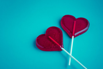 Red heart-shaped lollipop on a colored plain background