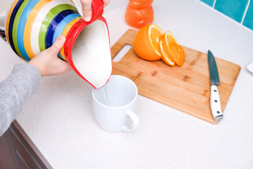 the boy pours water from a jug into a mug