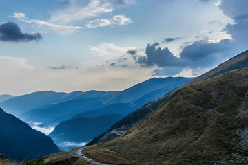 Obraz premium Cars passing on curvy mountain road with foggy forest landscape in the background