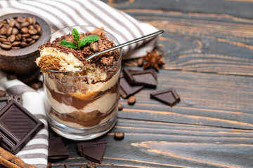 Classic tiramisu dessert in a glass cup and pieces of chocolate on wooden background