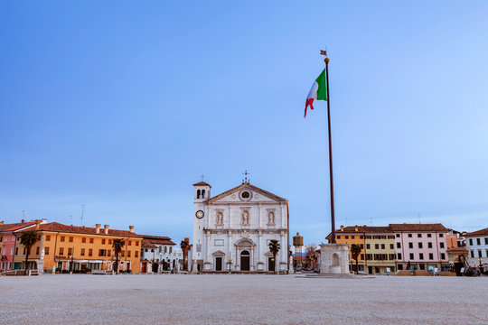 Duomo di Palmanova in piazza grande. Visibile il pennone con bandiera e il vecchio  serbatoio idrico a torre con cielo azzurro alla mattina.