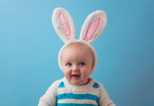 A happy baby with white easter bunny ears smiling at the camera