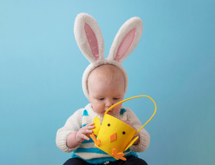 A baby wearig cute easter bunny ears peering into an easter chic basket